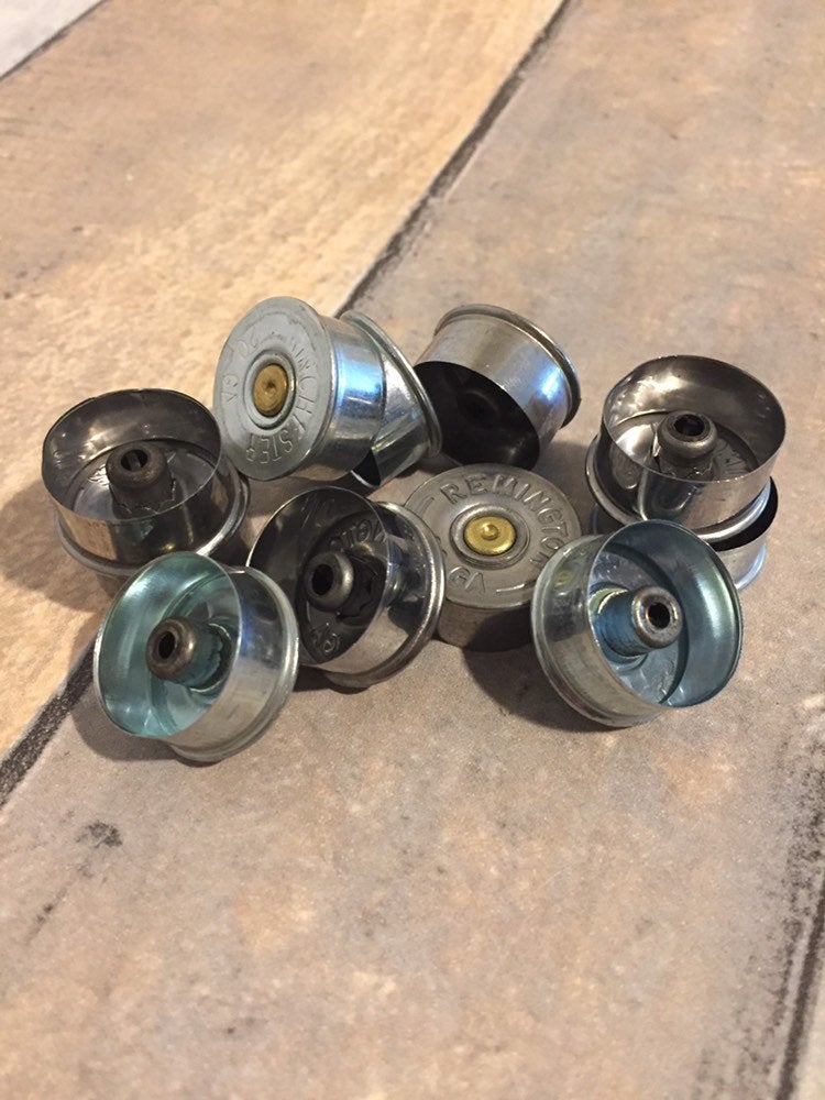 Ten silver 20 gauge shotgun shell brass end caps shown from the open cup side on a wood surface
