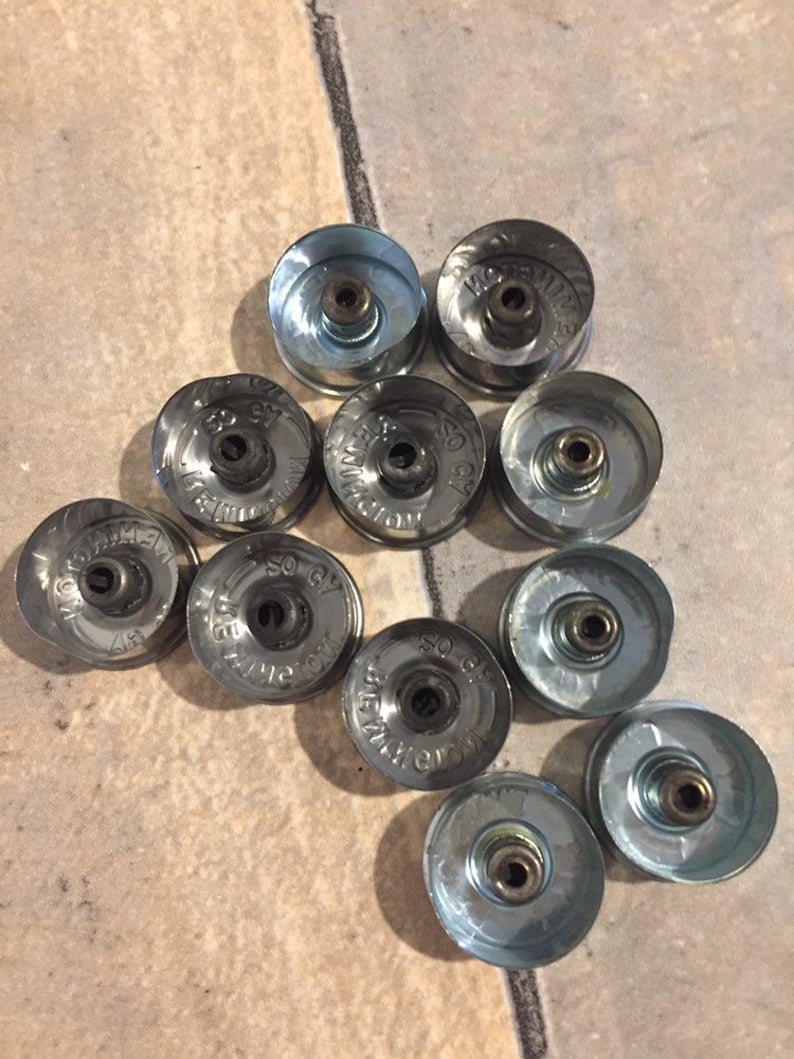 Ten silver 20 gauge shotgun shell brass end caps arranged in a cluster on a tile floor