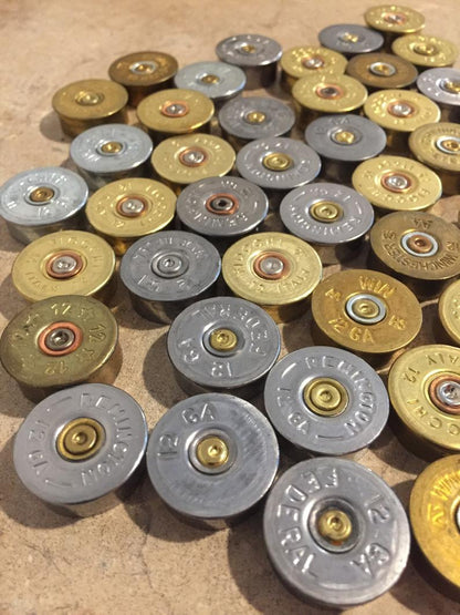A close-up view of numerous silver and gold-toned shotgun shell headstamps from various brands.
