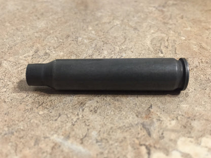 Side profile view of a single dark gray steel .223 casing resting horizontally on a beige stone surface.