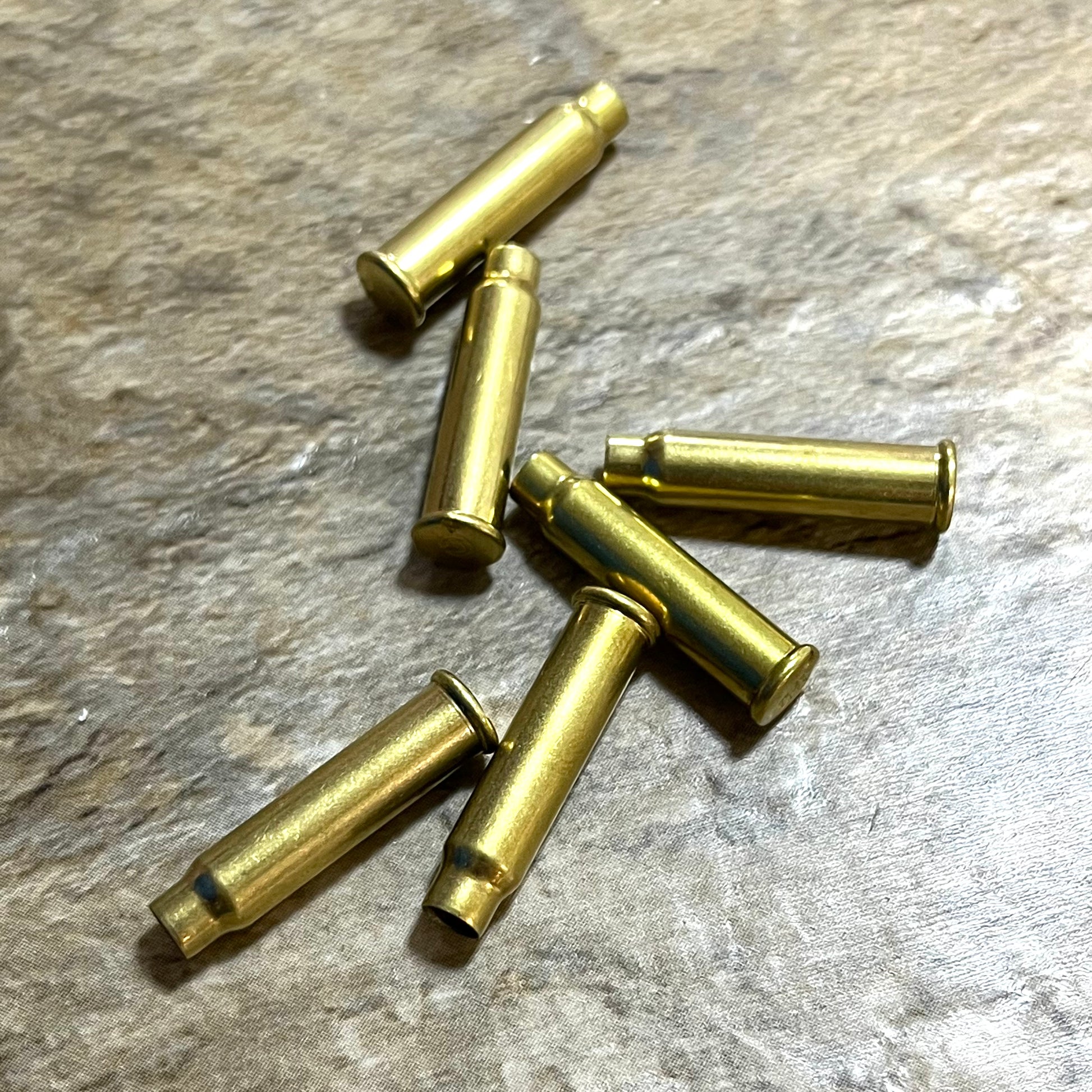 A small pile of six empty brass bullet casings arranged on a textured grey stone surface.