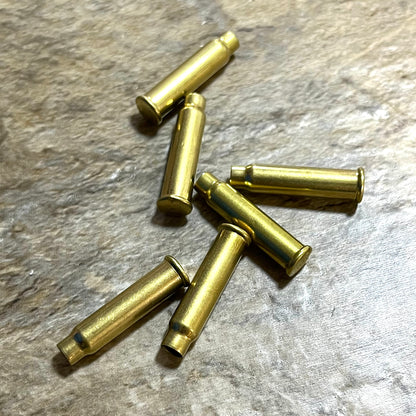 A small pile of six empty brass bullet casings arranged on a textured grey stone surface.