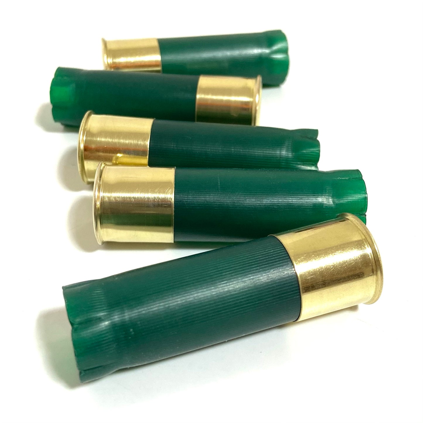 Five empty green shotgun shells four wedding boutonnieres with shiny brass bases arranged horizontally on a white background.