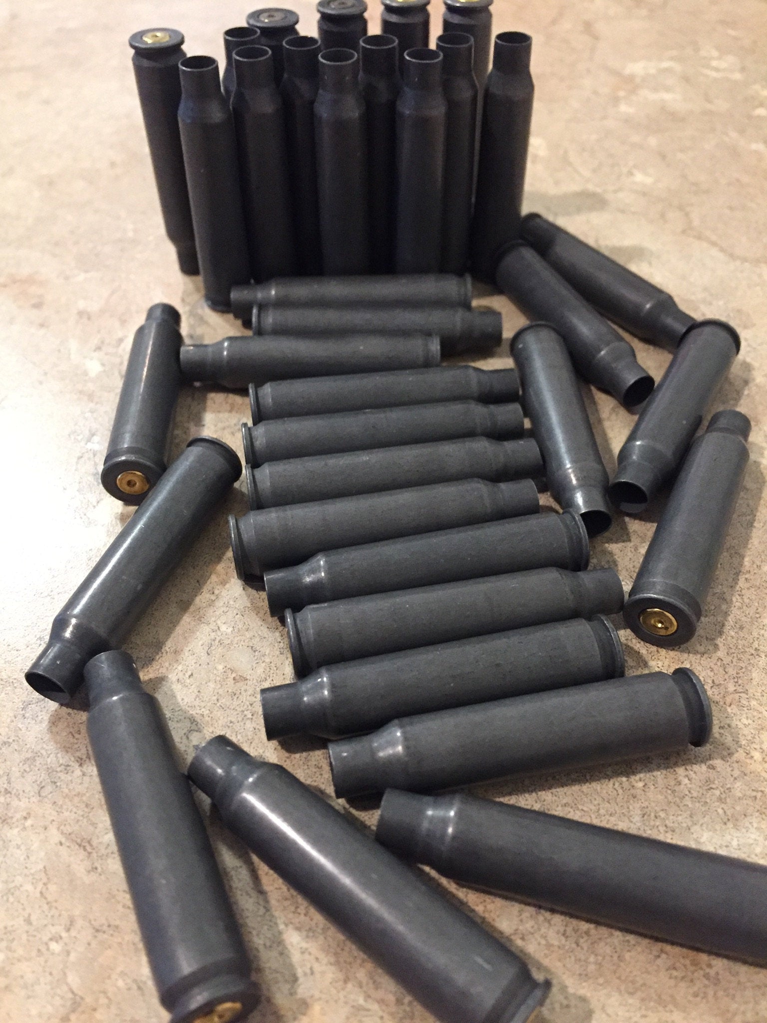 Dark gray steel 5.56 shells arranged in flat and upright rows on a stone surface showing open mouths and brass primers.