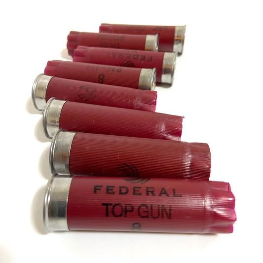 Six dark red 12 gauge Federal Top Gun shotgun hulls stacked diagonally showing silver bases and black branding.
