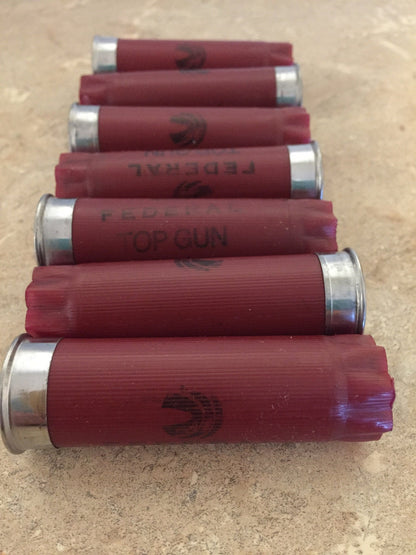 Six dark red shotgun shells lying horizontally stacked vertically on top of each other on a concrete surface.