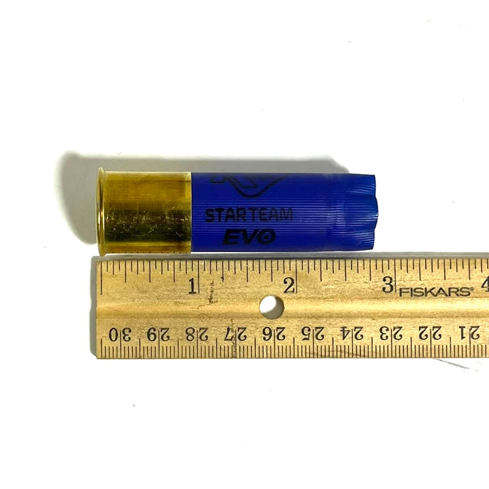 A single blue empty 12ga shell with Starteam Evo text, measured horizontally against a wooden ruler.