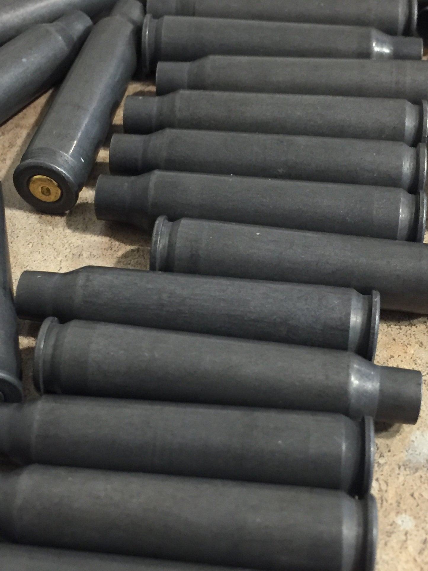 Close-up view of dark gray steel .223 cartridges stacked together showing brass primer pockets and rims.