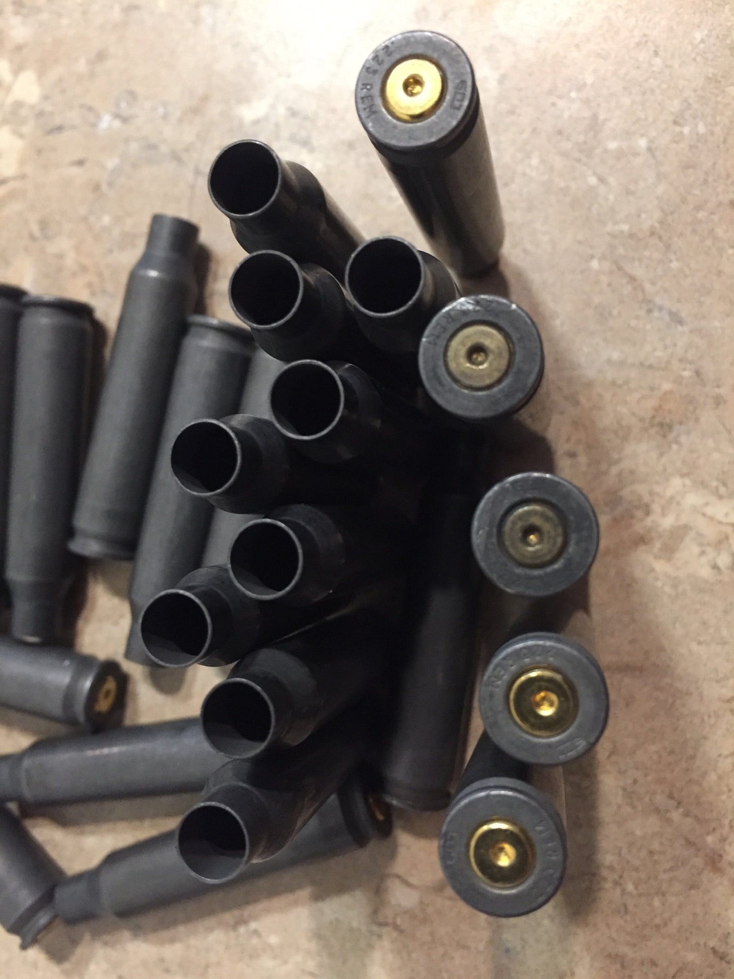 Dark gray steel .223 casings lined up on stone showing gold-colored brass primers alongside open casing mouths.