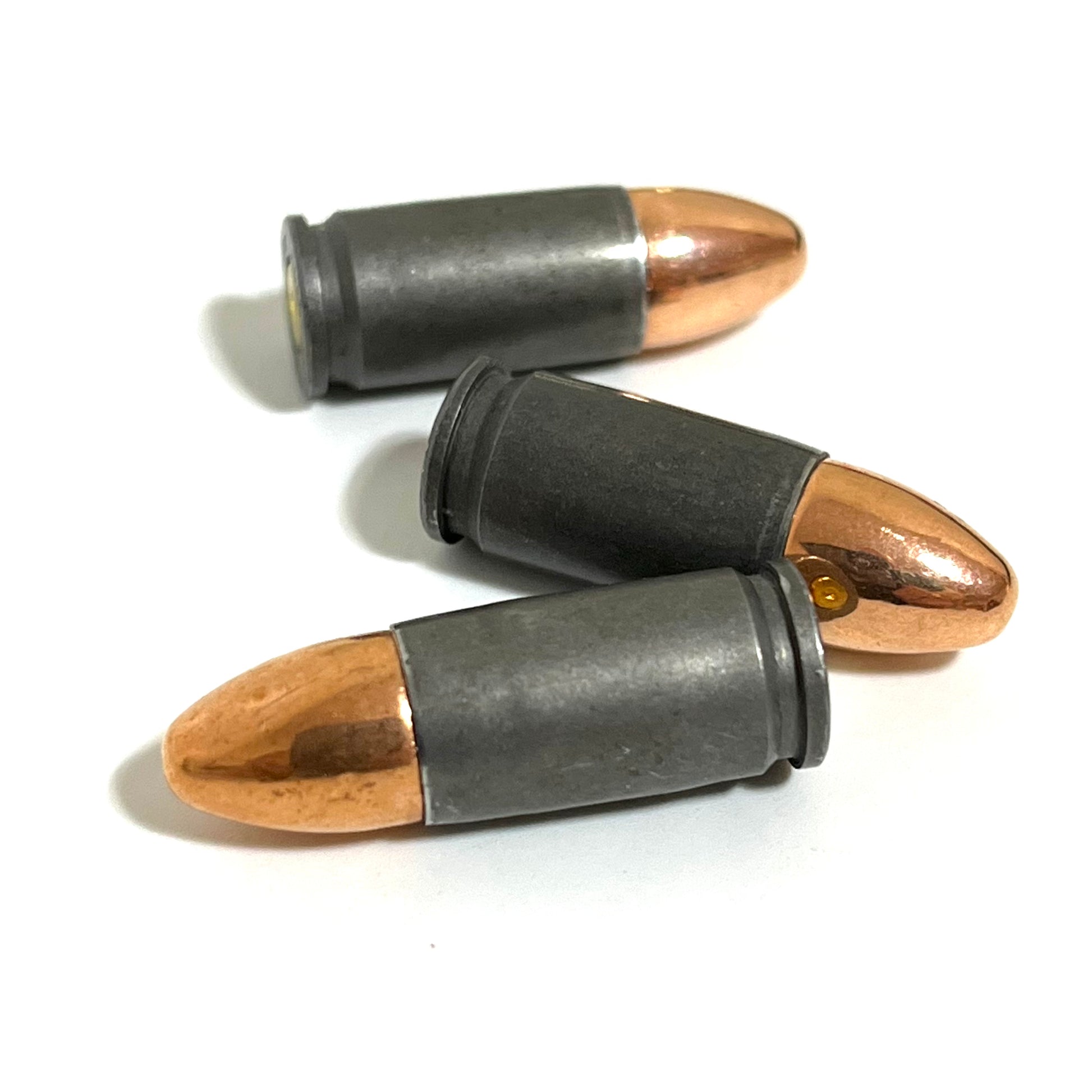 Three gray steel 9mm dummy cartridges lying on their sides in close-up with one gold primer visible