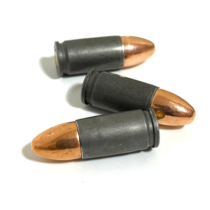 Three gray steel 9mm dummy cartridges lying on their sides in close-up with one gold primer visible