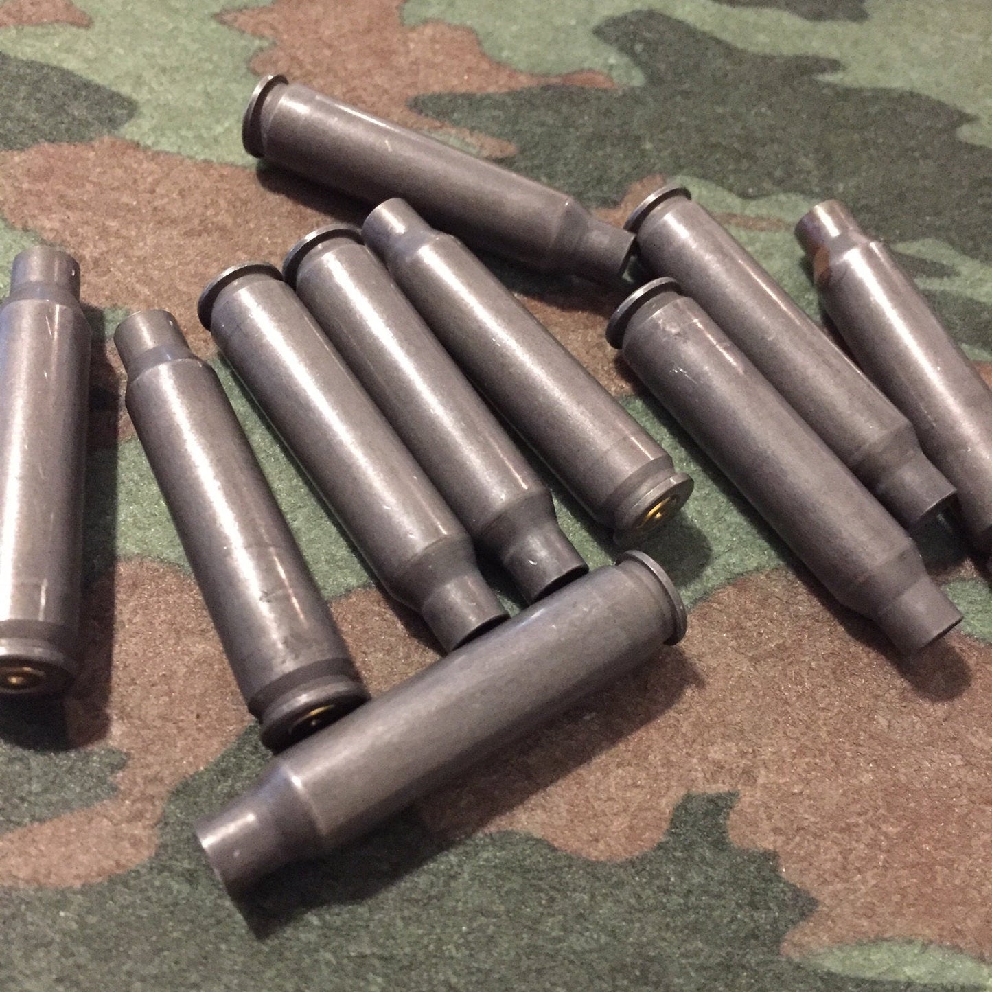 A loose heap of dark gray steel .223/5.56 empty cases crossed together on a camouflage background