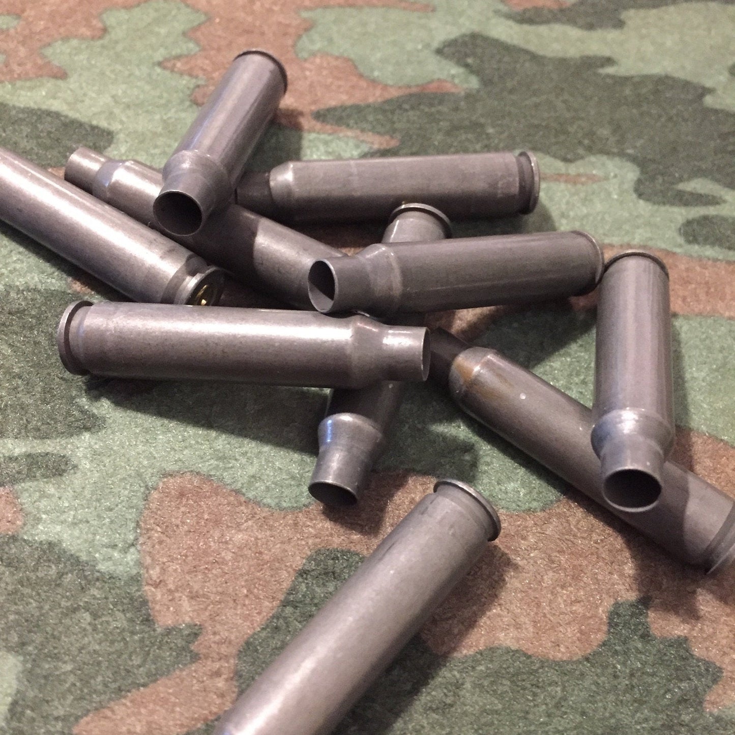 A scattered pile of dark gray steel .223/5.56 empty casings on a camouflage background