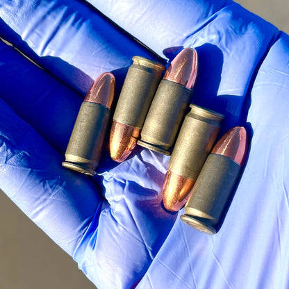Five gray steel 9mm dummy rounds fanned out in a blue nitrile-gloved hand
