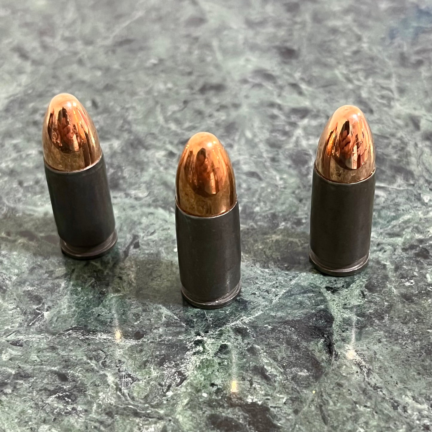 Three gray steel 9mm dummy rounds standing upright on a green marble surface