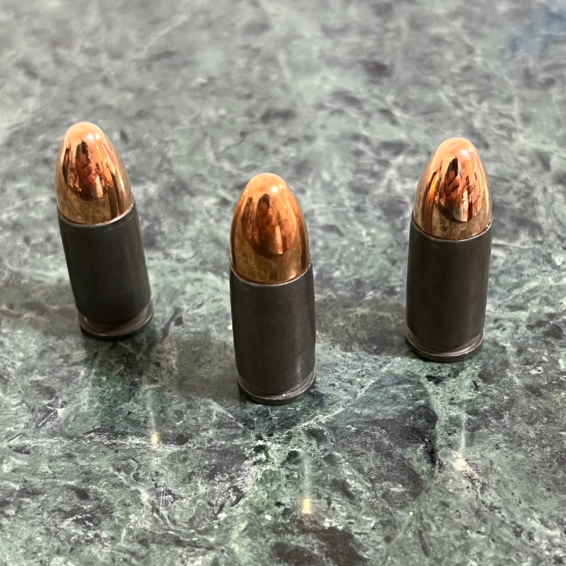 Three gray steel 9mm dummy rounds standing upright on a green marble surface