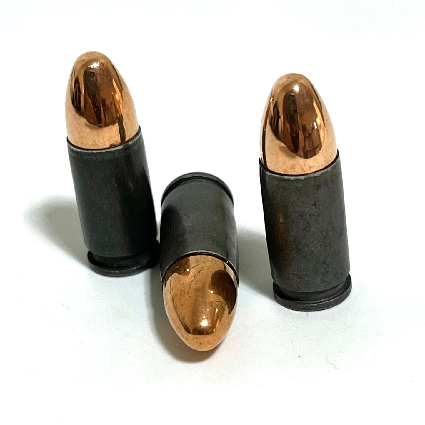 Three gray steel 9mm dummy rounds, two standing and one lying, shown without any text overlay