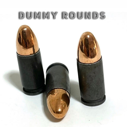 Three gray steel 9mm dummy rounds with round-nose copper bullets, two standing and one lying flat