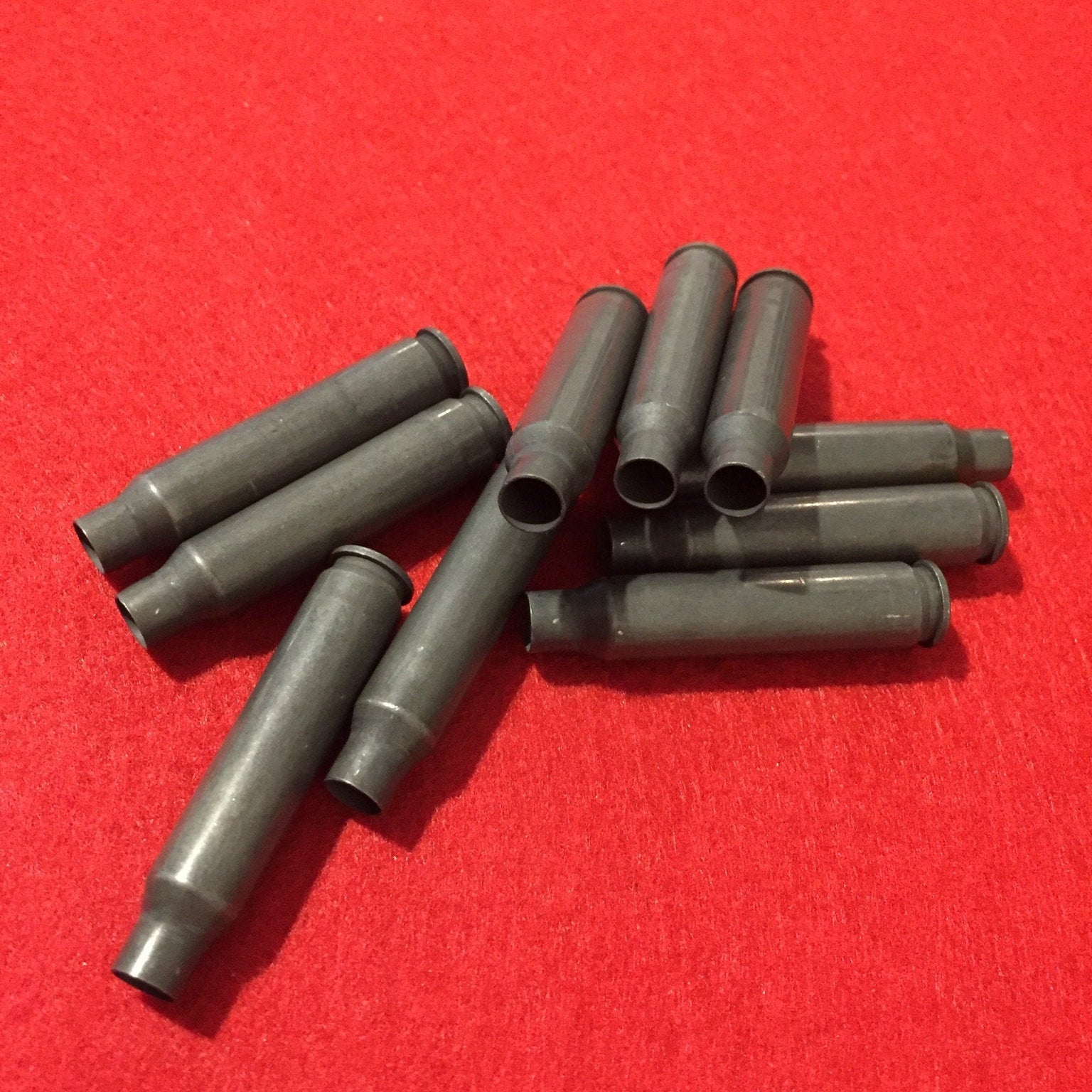 A small pile of dark gray steel .223/5.56 empty shells scattered on a red fabric background