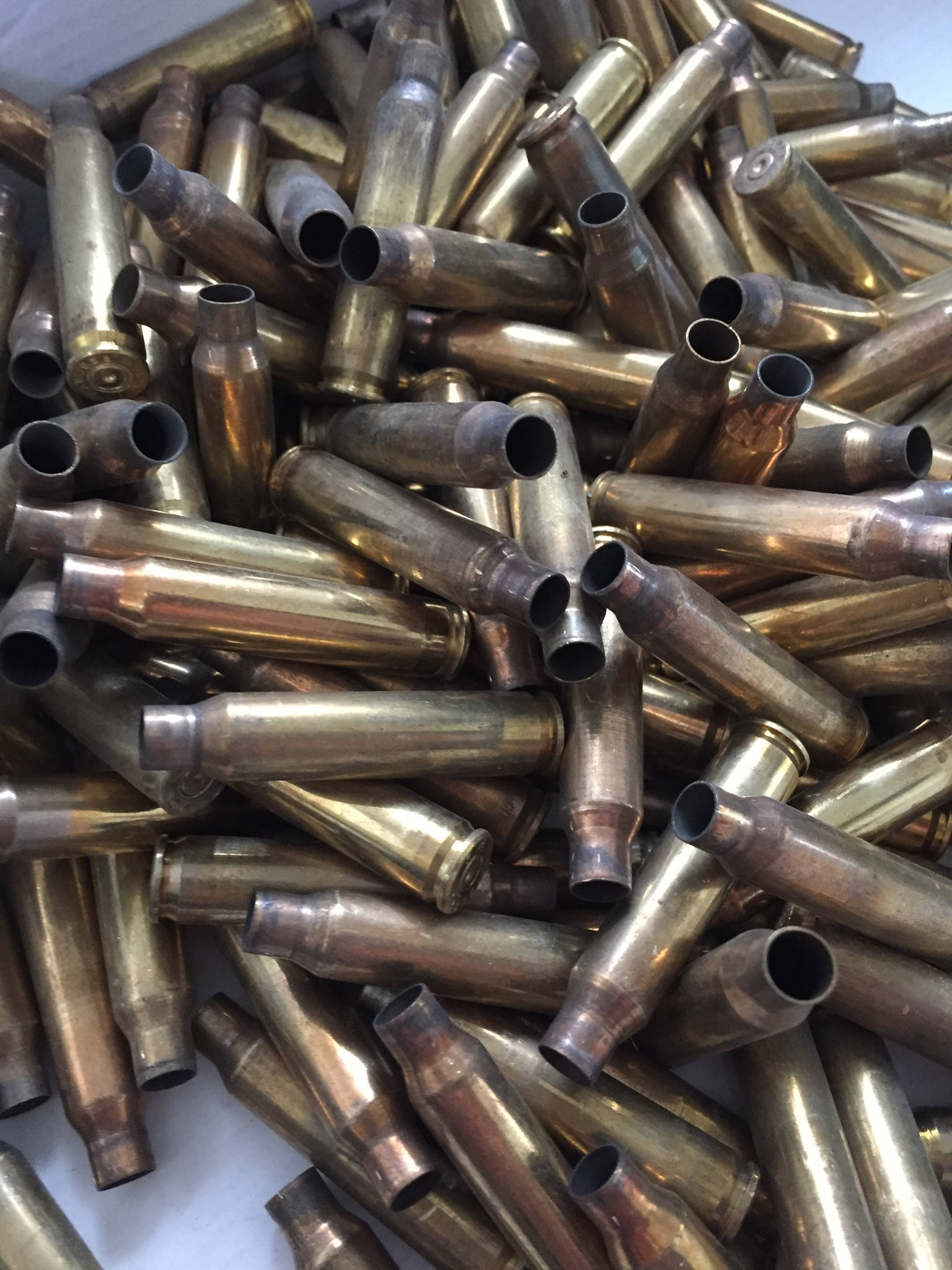 Close-up of a dense, jumbled pile of uncleaned .223 and 5.56 spent brass casings, showing heavy tarnish and dark spots.