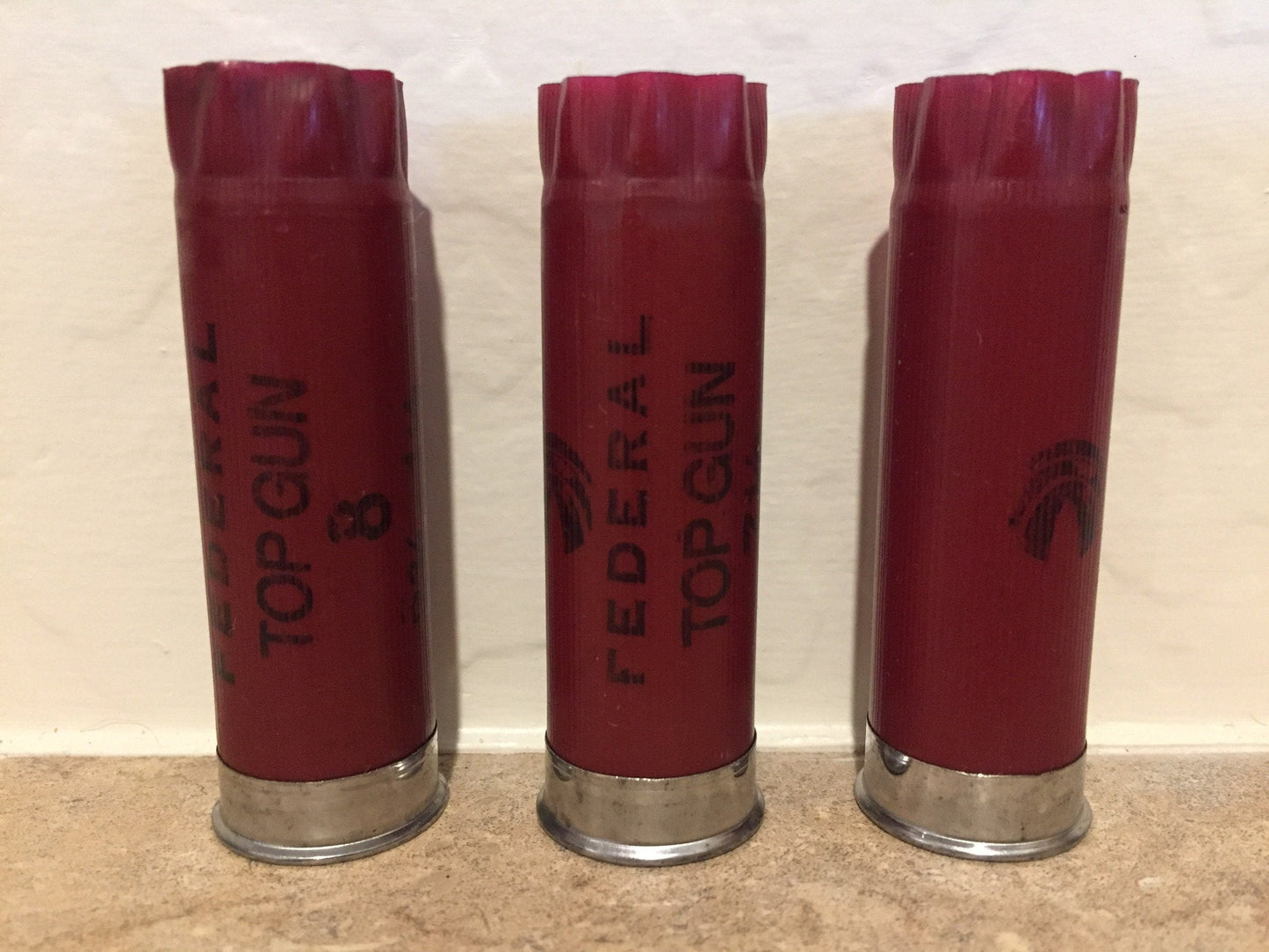Three dark red 12 gauge empty shotgun shells standing vertically side by side showing Federal Top Gun text.