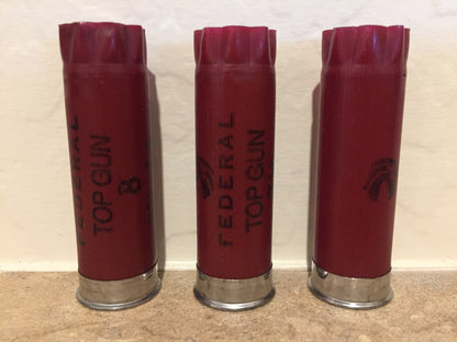 Three dark red 12 gauge empty shotgun shells standing vertically side by side showing Federal Top Gun text.