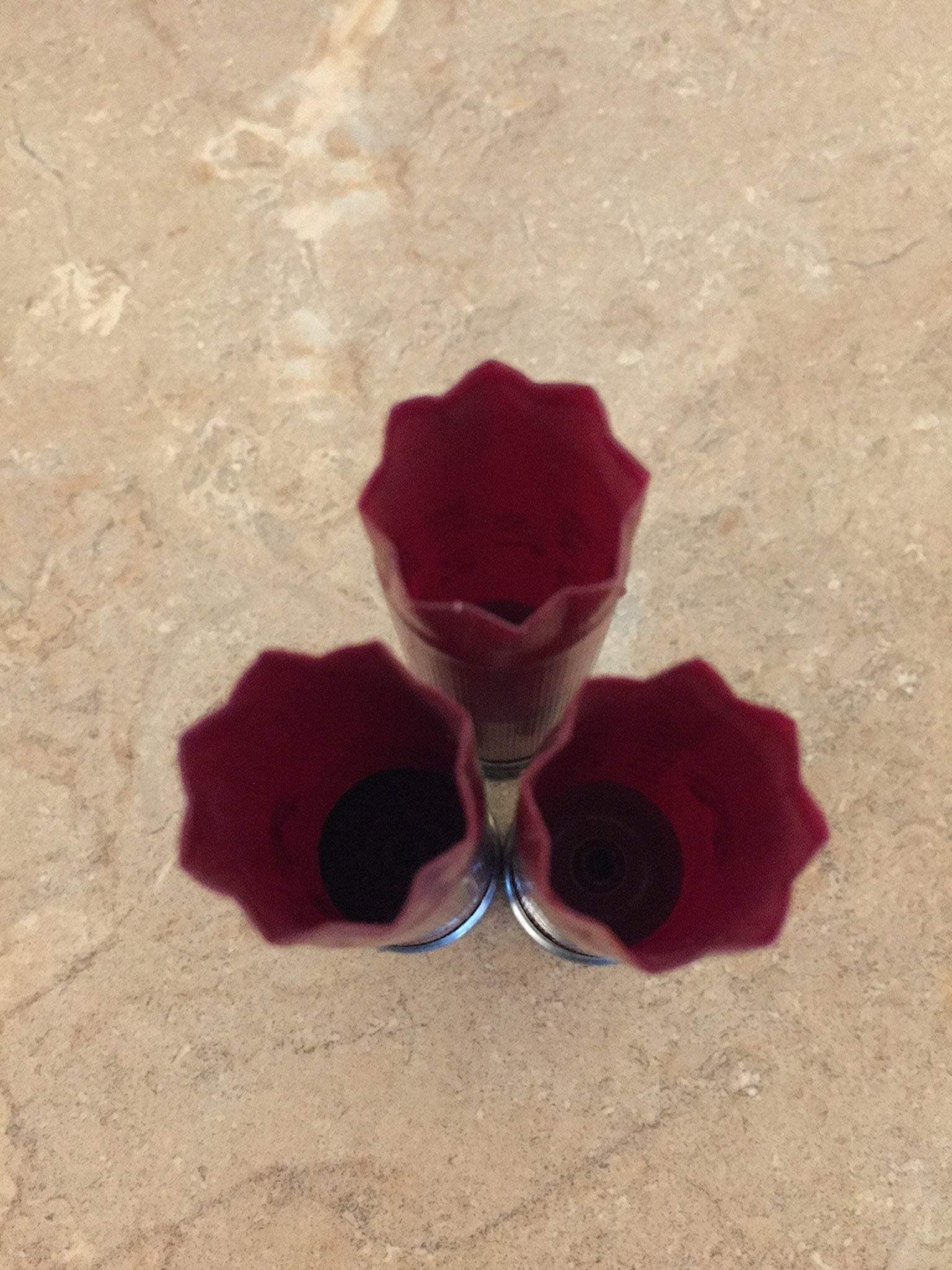 Three empty burgundy 12ga cartridges standing upright on a textured surface.