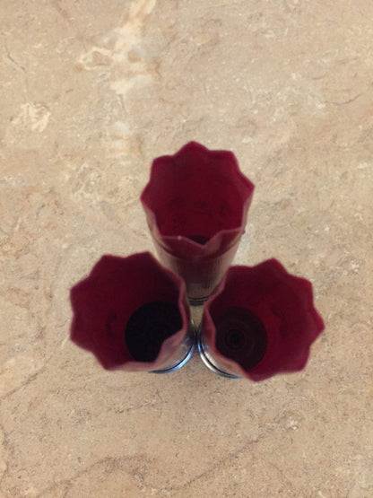 Three empty burgundy 12ga cartridges standing upright on a textured surface.