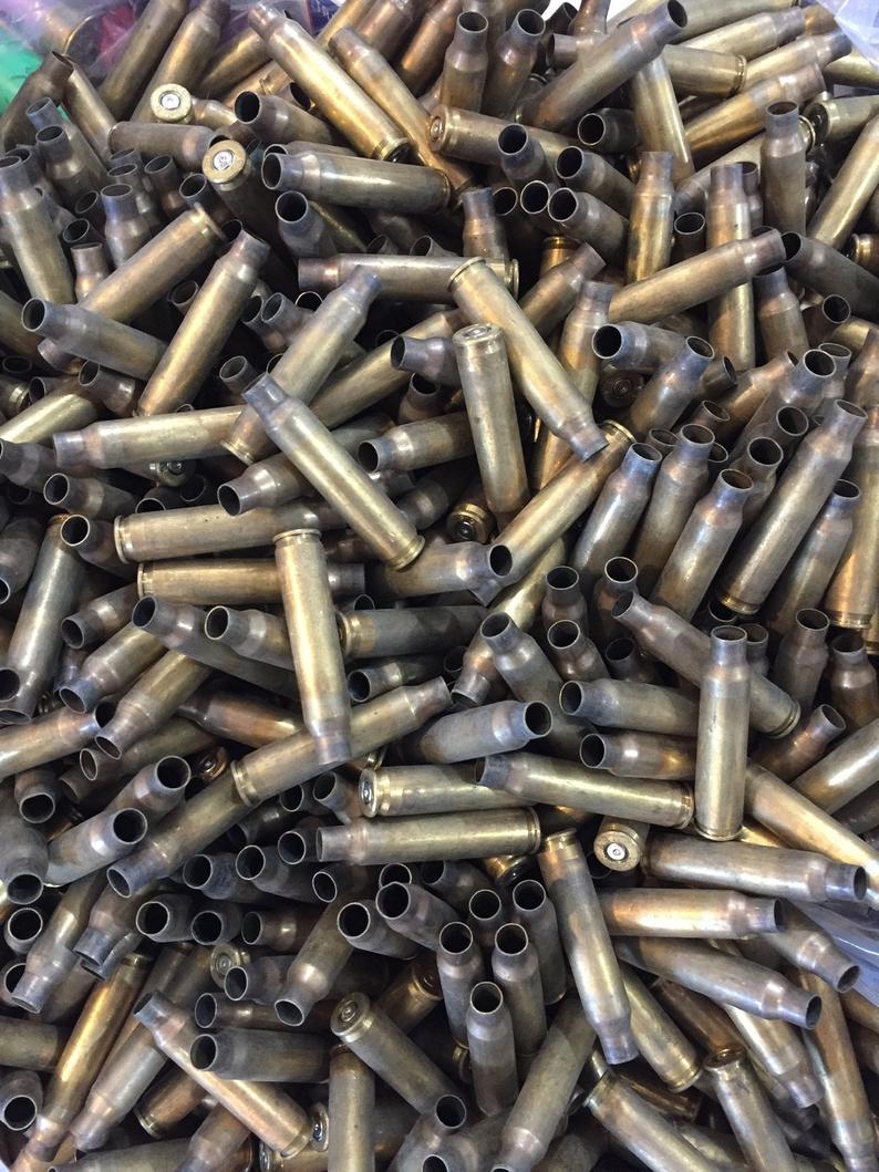 Top-down view into a container filled with a large, uncounted bulk pile of dirty, spent .223 and 5.56 brass casings.