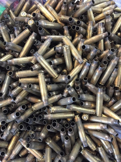 Top-down view into a container filled with a large, uncounted bulk pile of dirty, spent .223 and 5.56 brass casings.