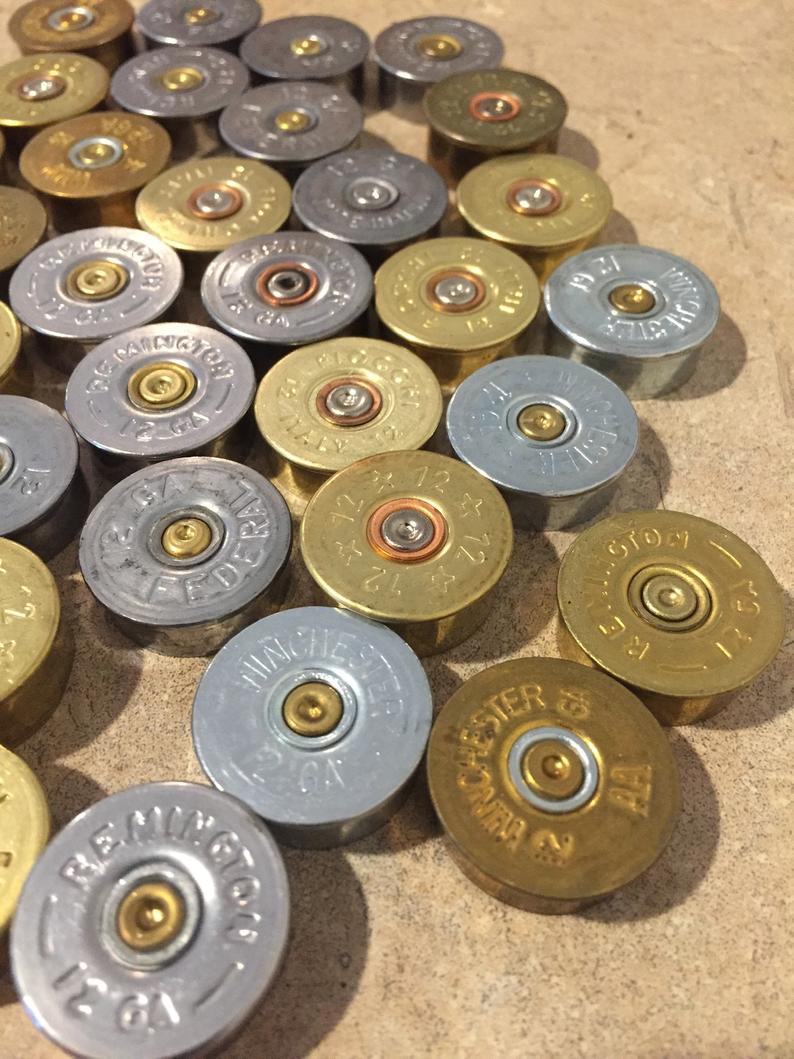 A top-down view of a collection of mixed gold and silver 12 gauge shotgun shell headstamps with different colored inert primers.
