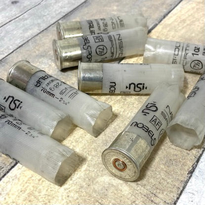 Six semi-translucent Nobel 12 gauge high brass shotgun shells scattered on a wood surface