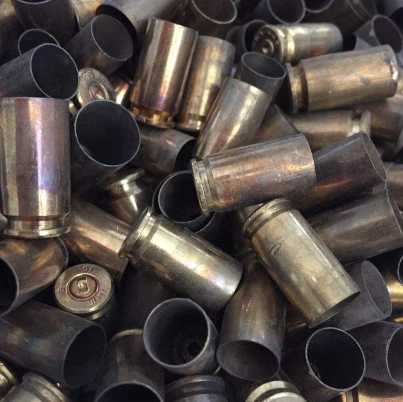 Macro close-up pile of uncleaned 9mm brass casings showing discolored sidewalls, hollow mouths, and a stamped base.