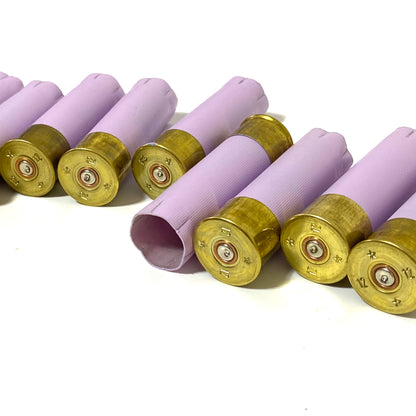 Row of lavender purple 12 gauge shotgun shells with gold bases lying at an angle showing headstamps