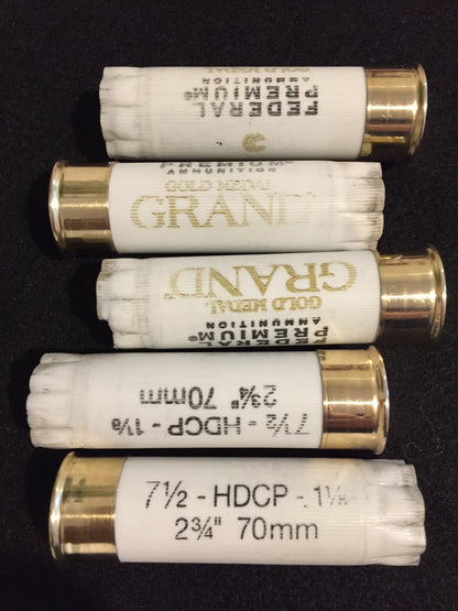 Five white empty shotgun shells with gold brass bottoms arranged horizontally on a black background.