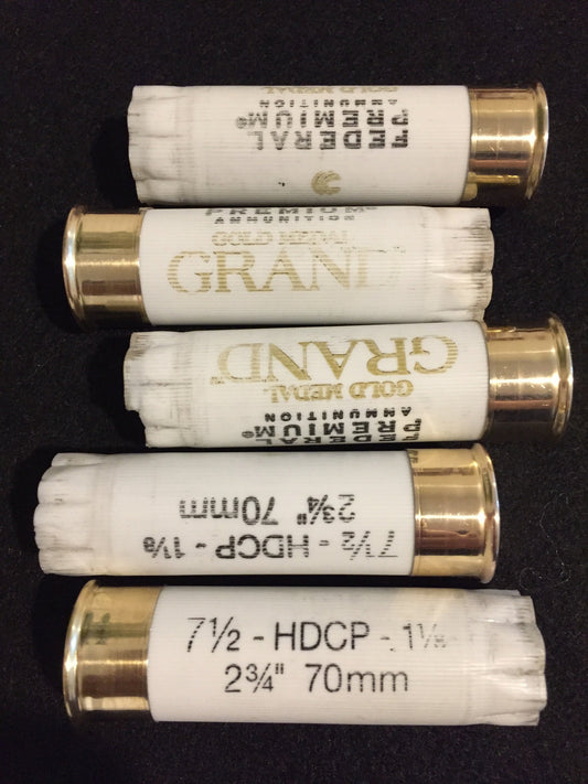 Five white empty shotgun shells with gold brass bottoms arranged horizontally on a black background.