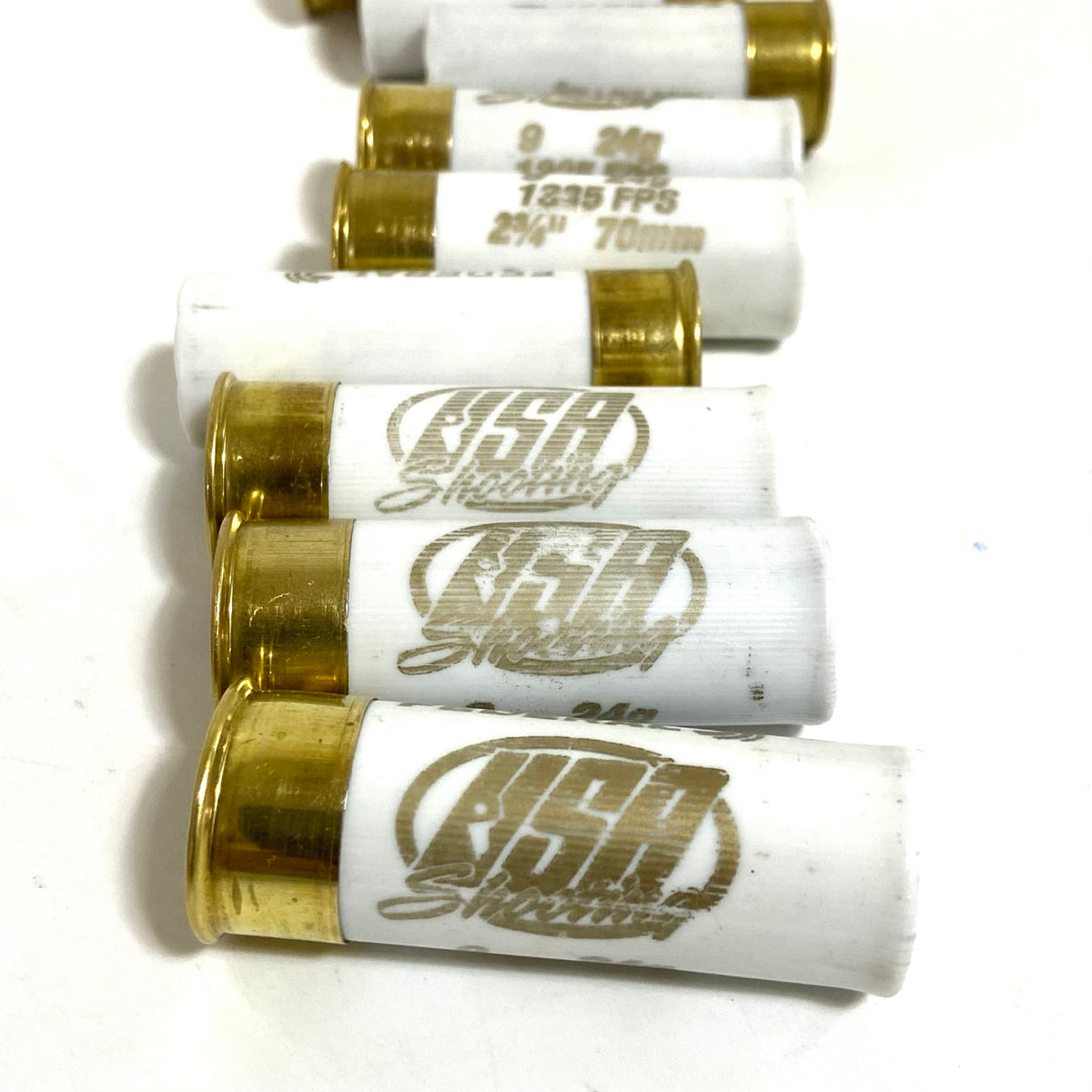 White empty shotgun shells lying in a diagonal row, gold brass bases and USA Shooting text visible on a light surface.