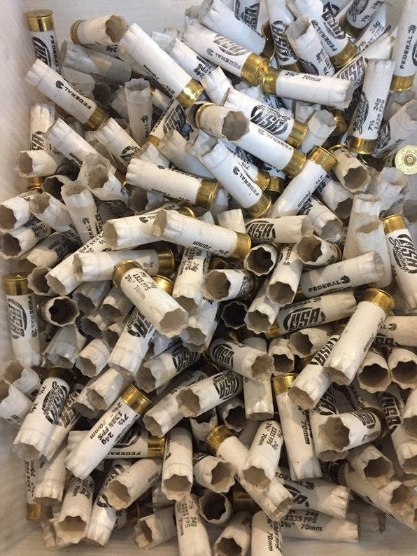 Large pile of empty white 12 gauge Federal and USA Shooting shotgun shells with brass bases in a cardboard box
