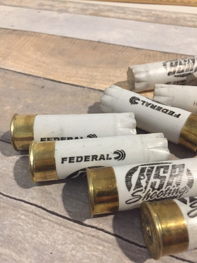 Pile of white Federal and USA Shooting 12 gauge shotgun shells with brass bases on a wood surface