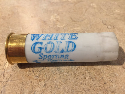 Single white shotgun shell with a brass base printed "White Gold Sporting 70mm" lying on a stone surface