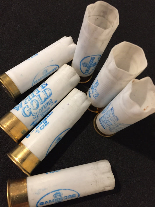 6 white shotgun shells with brass bases lying at angles showing "White Gold Sporting" and "Gamebore" printed text