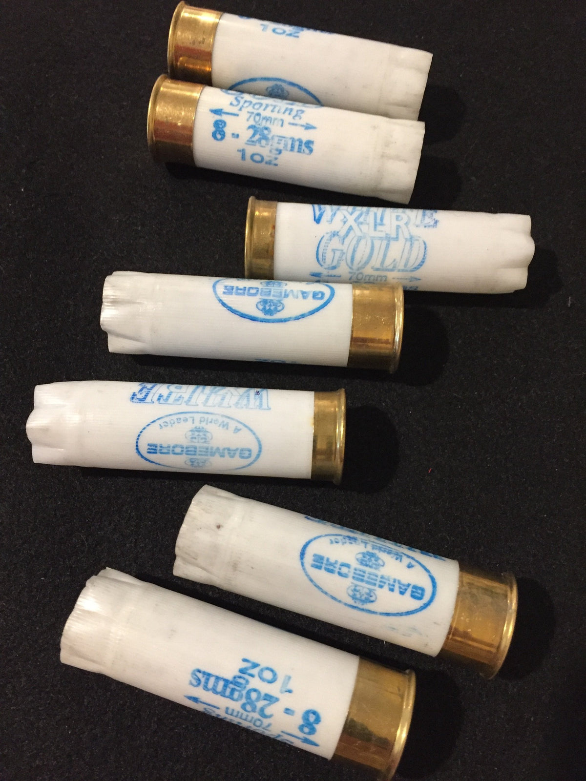 7 white shotgun shells with brass bases lying on their sides in rows showing "Gamebore" and "White Gold" printed text