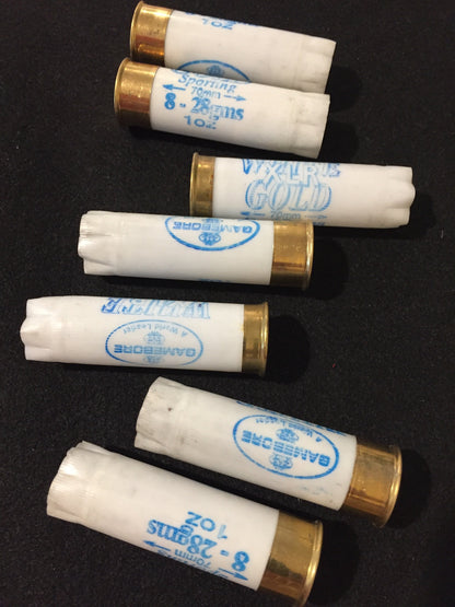 7 white shotgun shells with brass bases lying on their sides in rows showing "Gamebore" and "White Gold" printed text