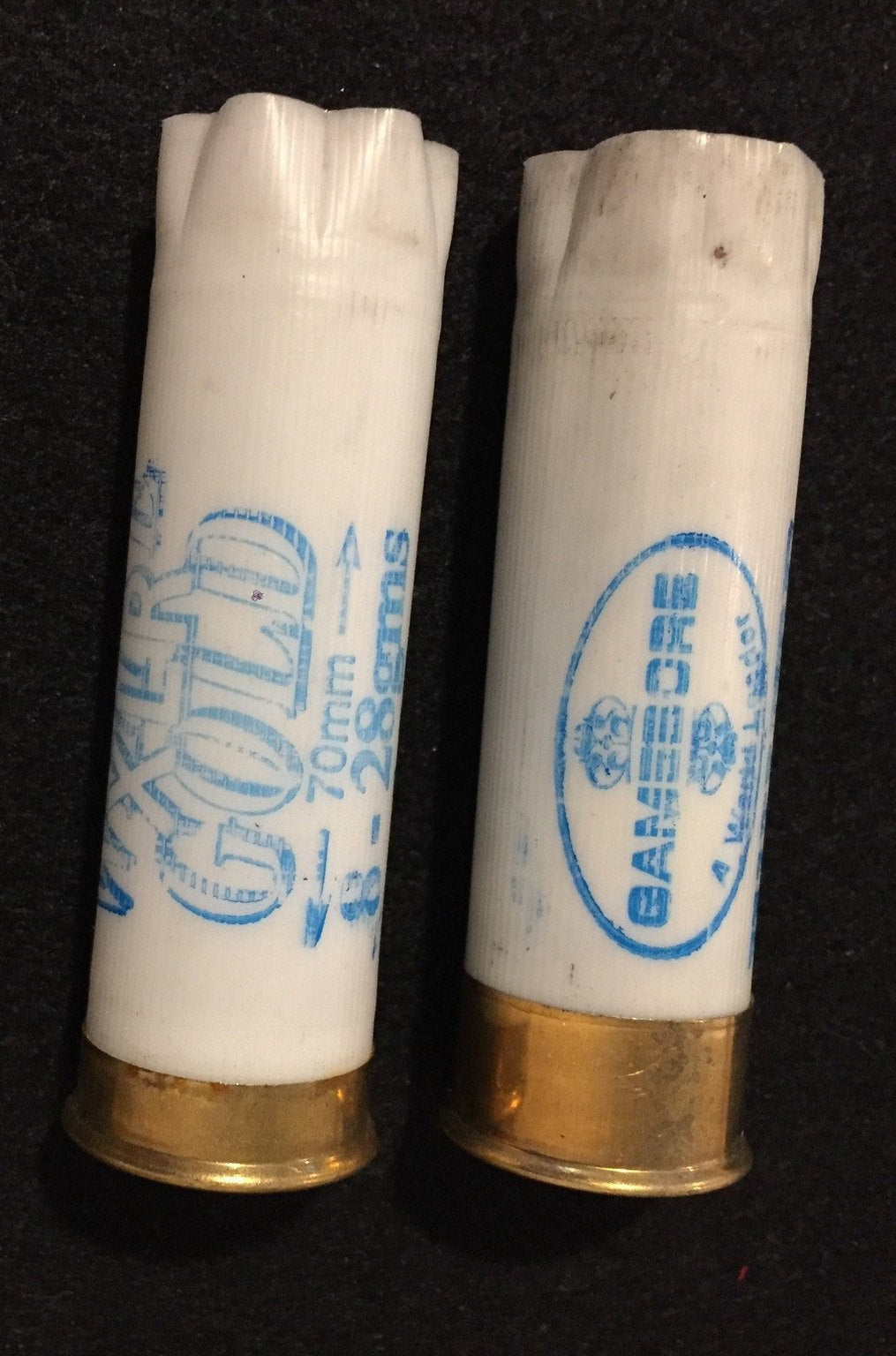 2 white shotgun shells with brass bases standing upright showing "White Gold" and "Gamebore" printed text