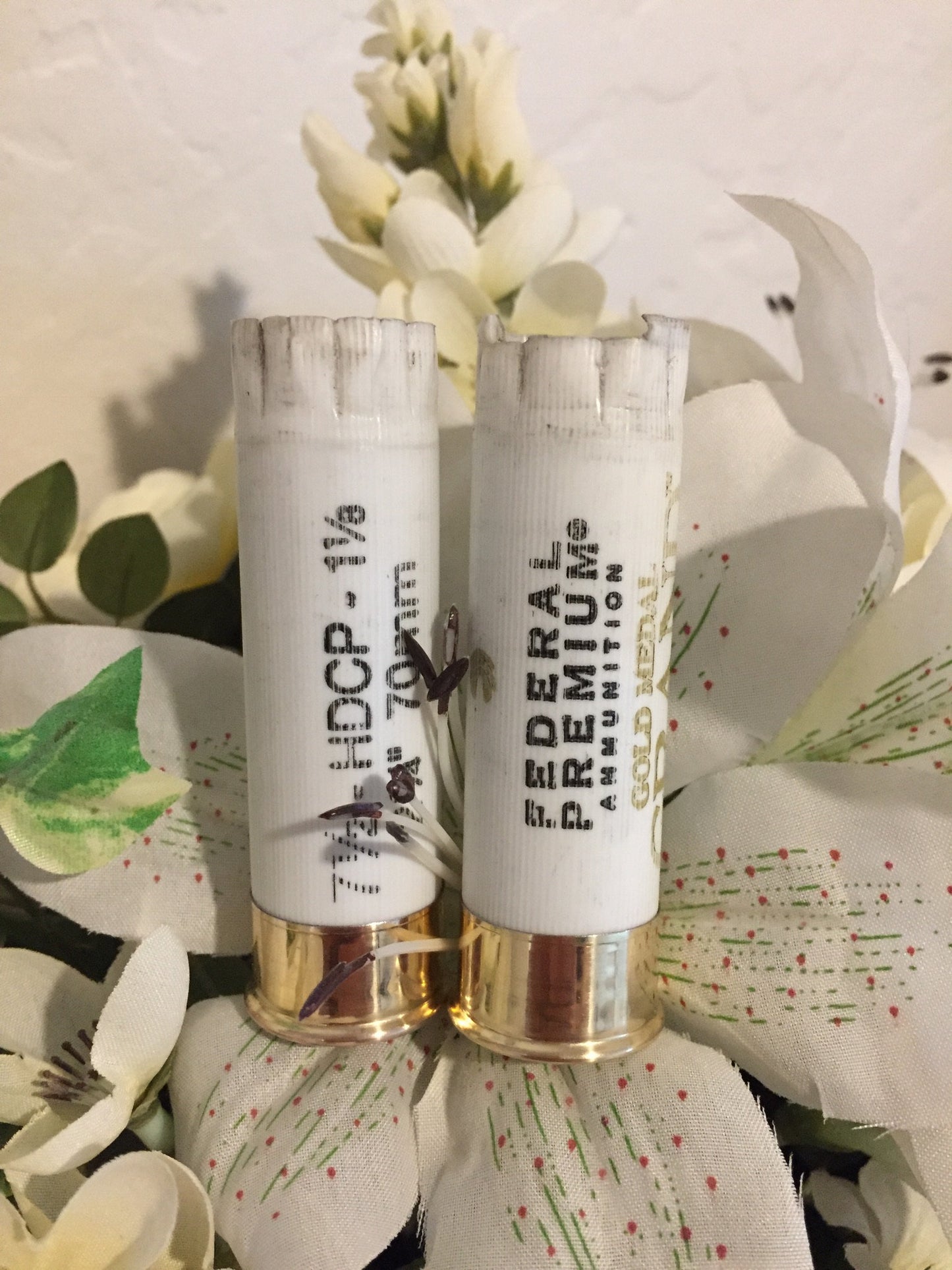 Two white shotgun hulls with gold bottoms standing vertically inside a white floral boutonniere arrangement.
