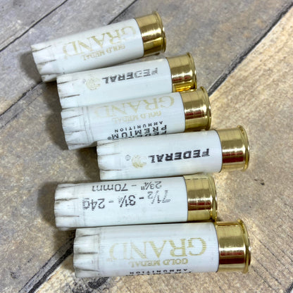 Five white spent casings with gold bottoms lying flat on a grey wooden surface.