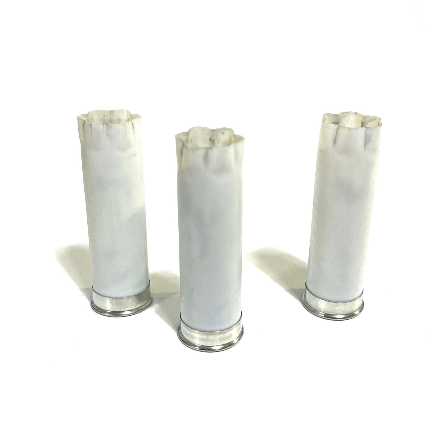 Three white spent shotgun hulls with frayed tops and silver bases standing on a white background