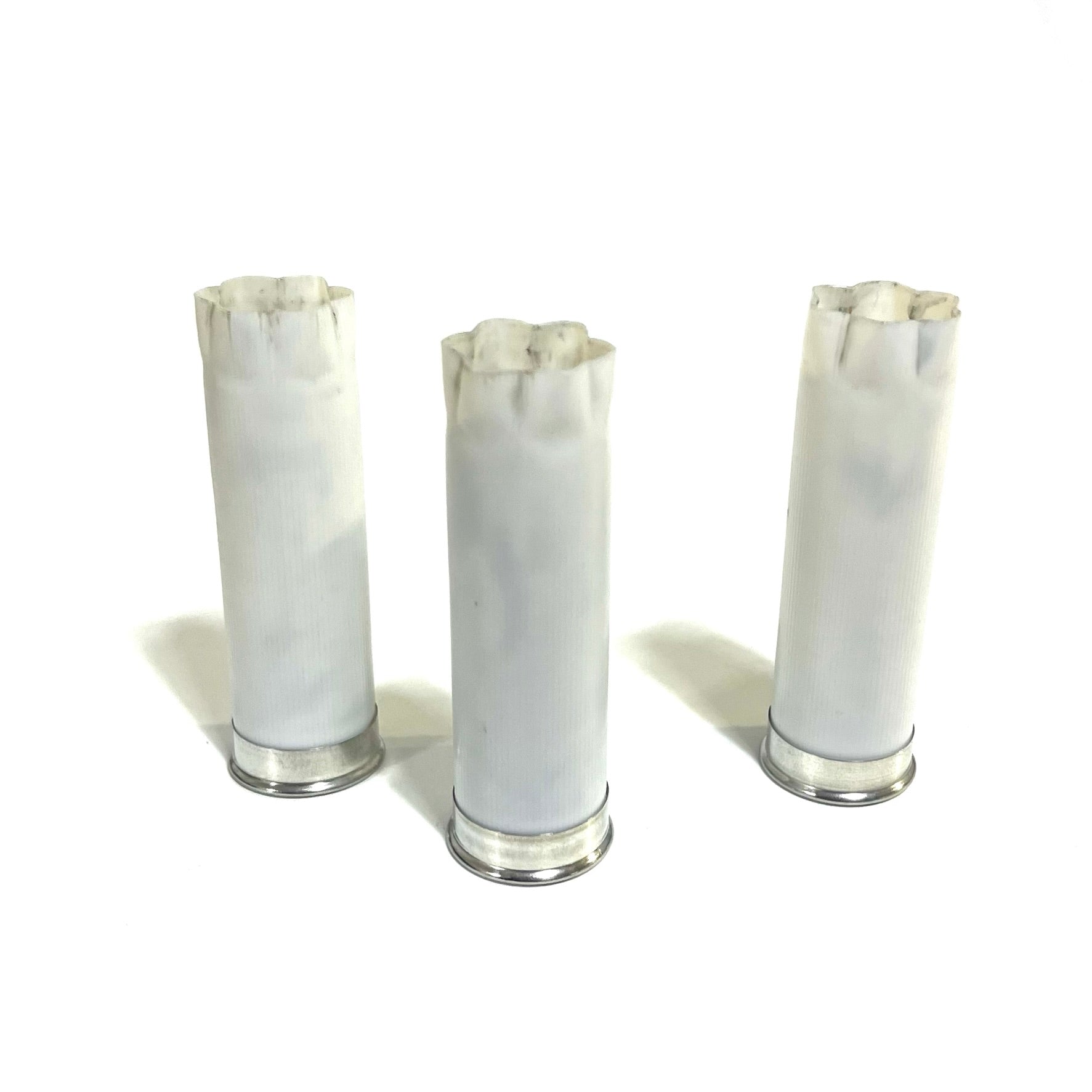 Three white spent shotgun hulls with frayed tops and silver bases standing on a white background