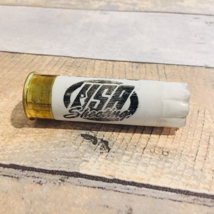 White 12 gauge shotgun shell with brass base printed USA Shooting lying on a wood plank surface