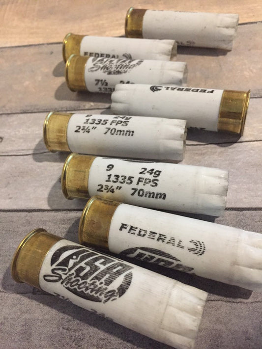 7 empty white 12 gauge Federal shotgun shells with brass bases and black printing arranged on a wood deck